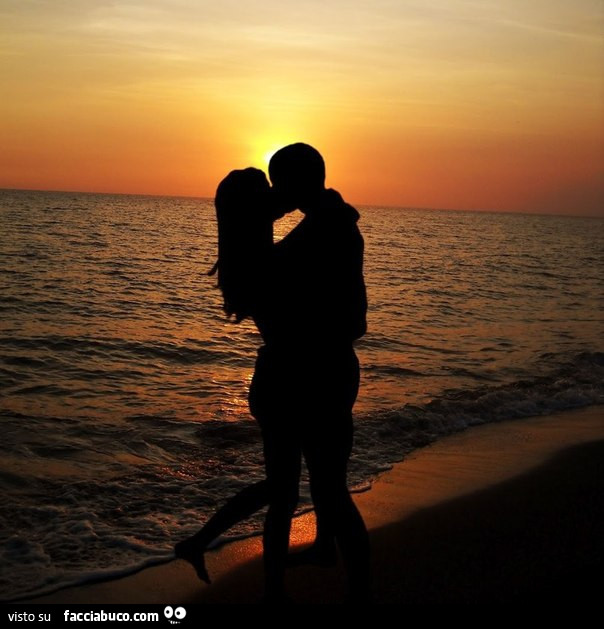 Coppia che si bacia sulla spiaggia al tramonto